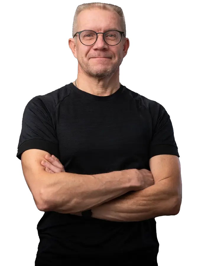 Mustapaitainen mieshenkilö katsoo kohti. Kädet ristissä rinnalla. Miehellä on silmälasit.