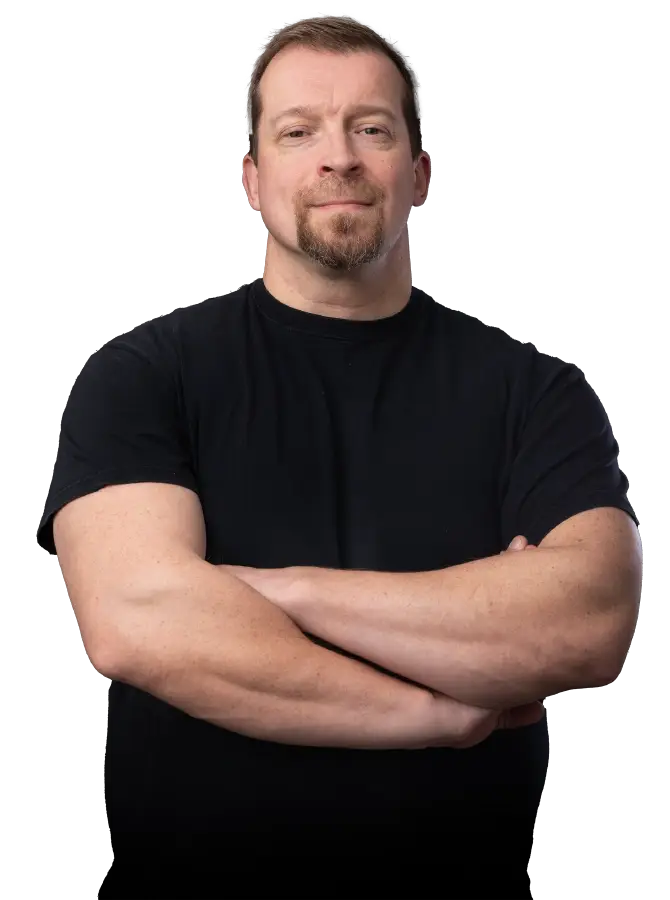 Mustapaitainen mieshenkilö katsoo kohti. Kädet ristissä rinnalla.