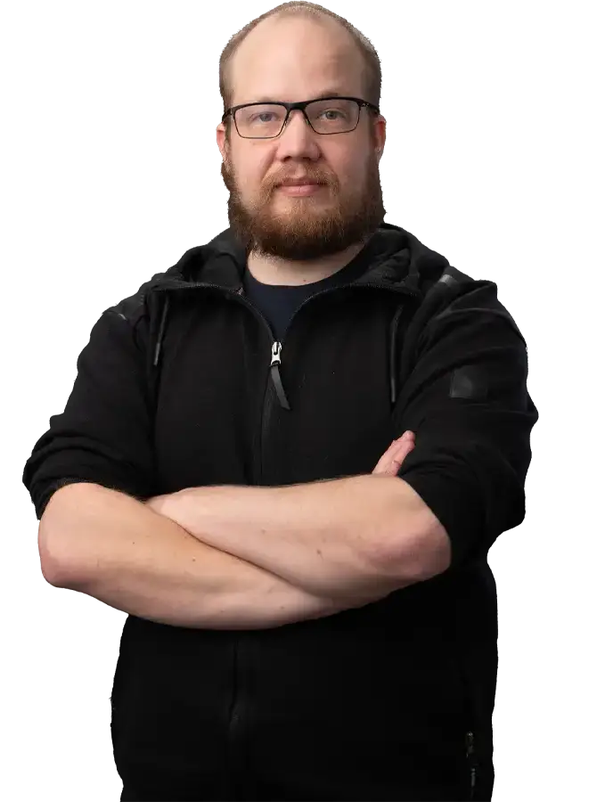 Mustapaitainen mieshenkilö katsoo kohti. Kädet ristissä rinnalla. Miehellä on silmälasit.