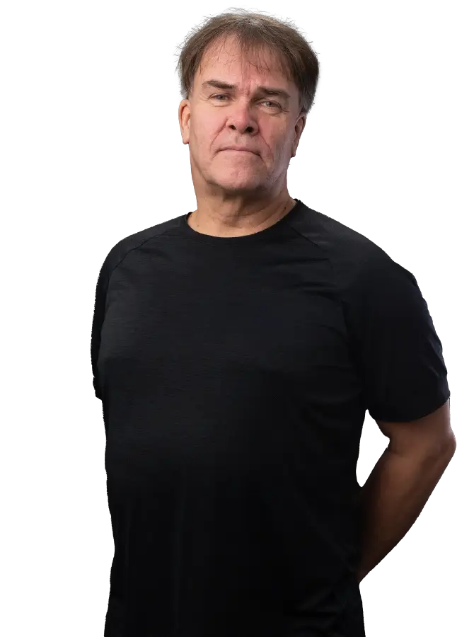 Mustapaitainen mieshenkilö katsoo kohti. Kädet selän takana.