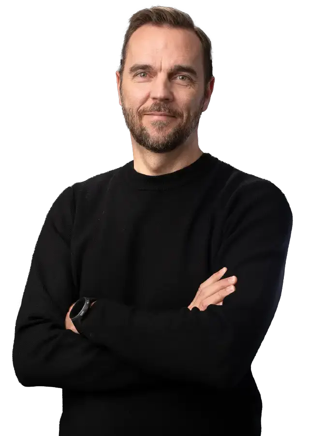 Mustapaitainen mieshenkilö katsoo kohti hymyillen ja kädet ristissä rinnalla.