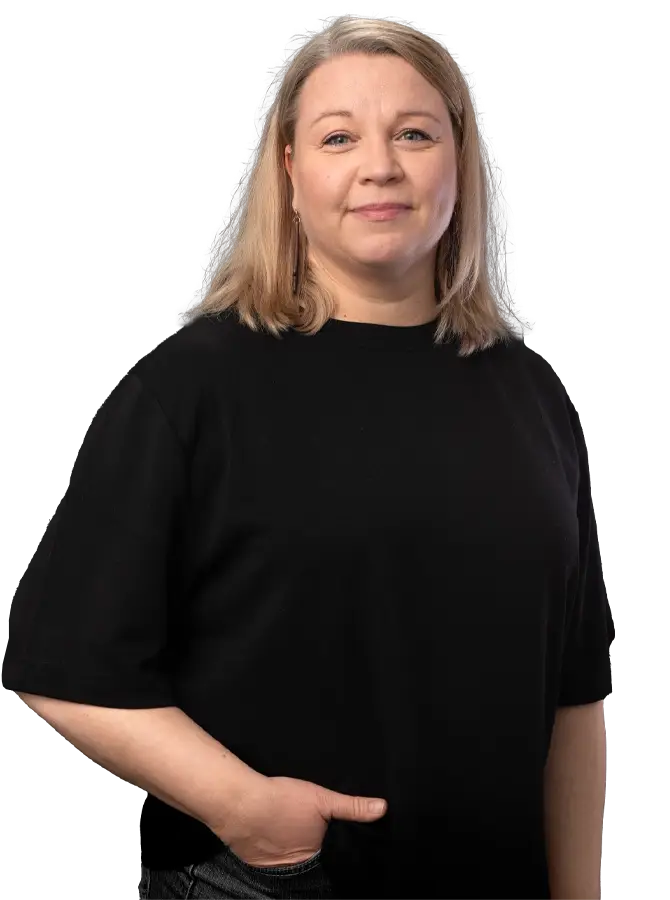 Mustapaitainen naishenkilö katsoo kohti. Toinen käsi housujen etutaskussa.