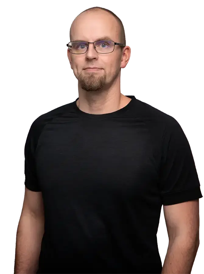 Mustapaitainen mieshenkilö katsoo kohti. Miehellä on silmälasit.