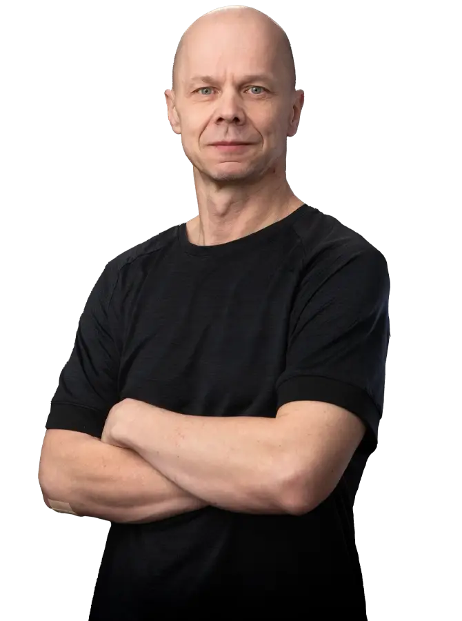 Mustapaitainen mieshenkilö katsoo kohti. Kädet rinnalla ristissä.